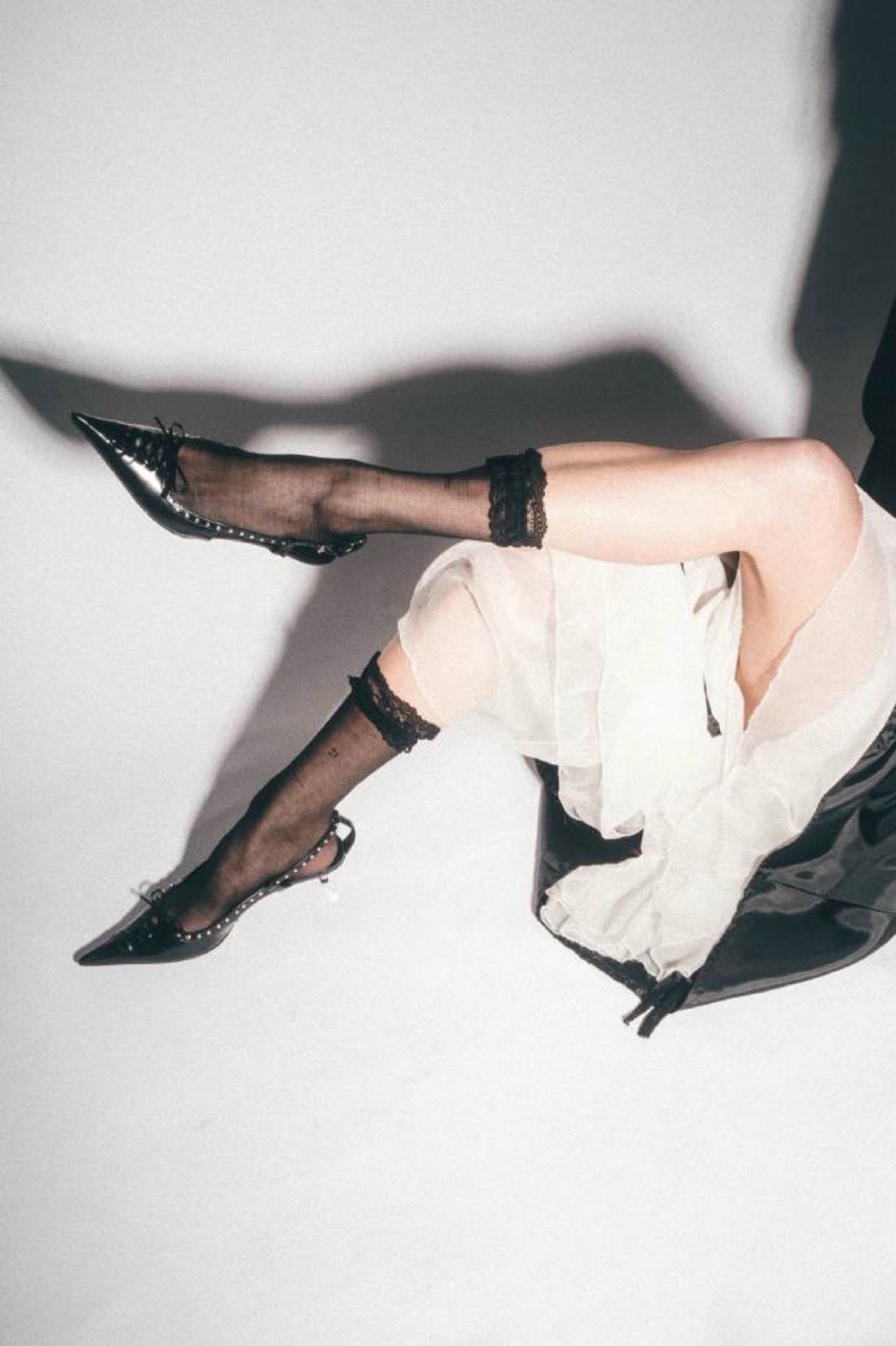 Legs in sheer black socks and pointed shoes under a white organza skirt
