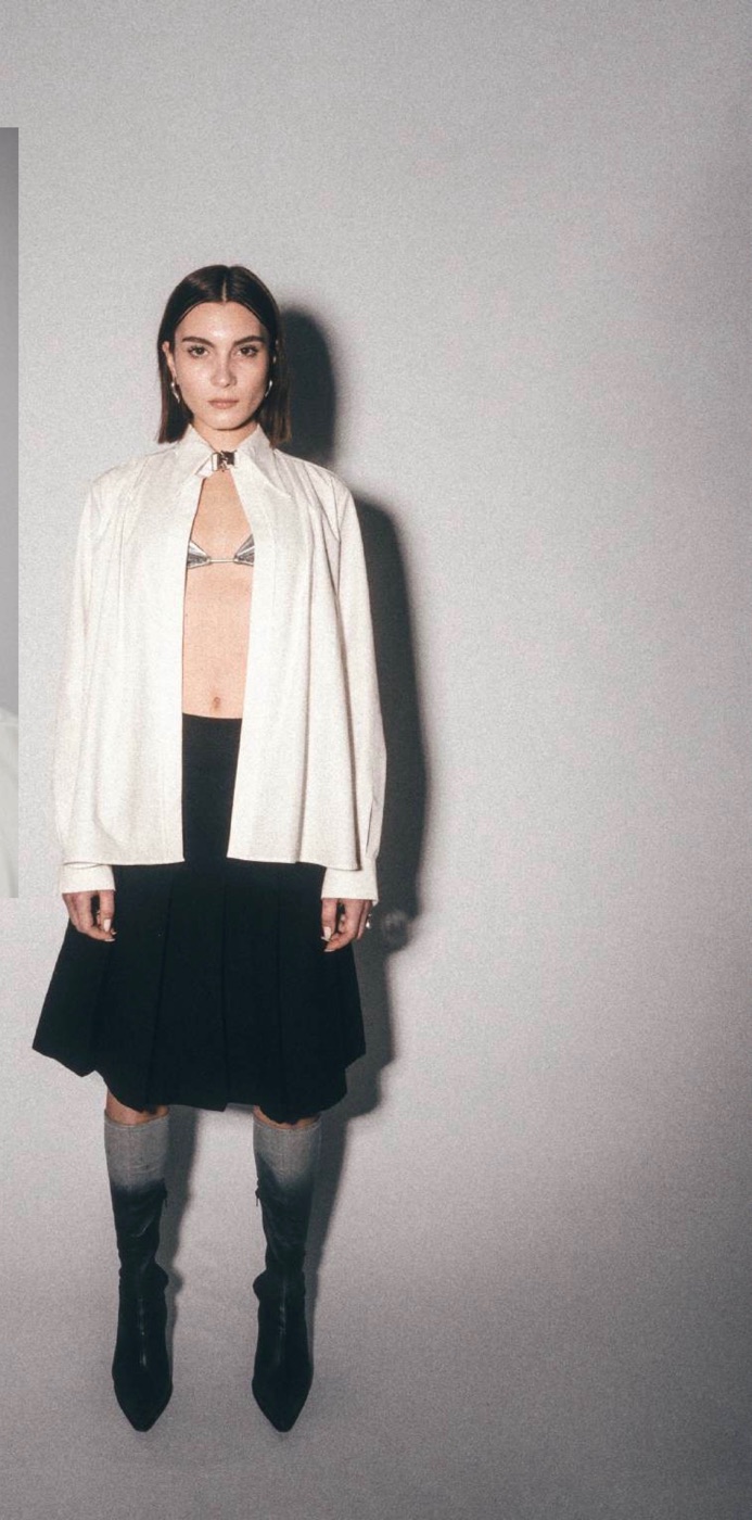 Model standing in the oversized white poplin shirt and pleated skirt