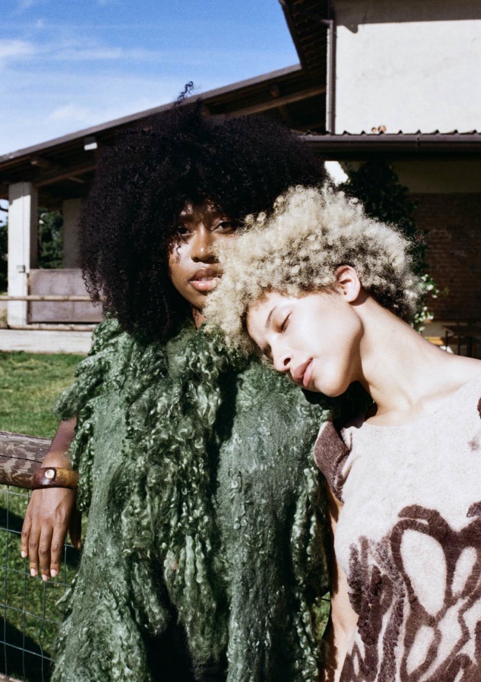 Two models outside a farmhouse, one in the moss-green felted piece, one in a felted top with brown organic patterns